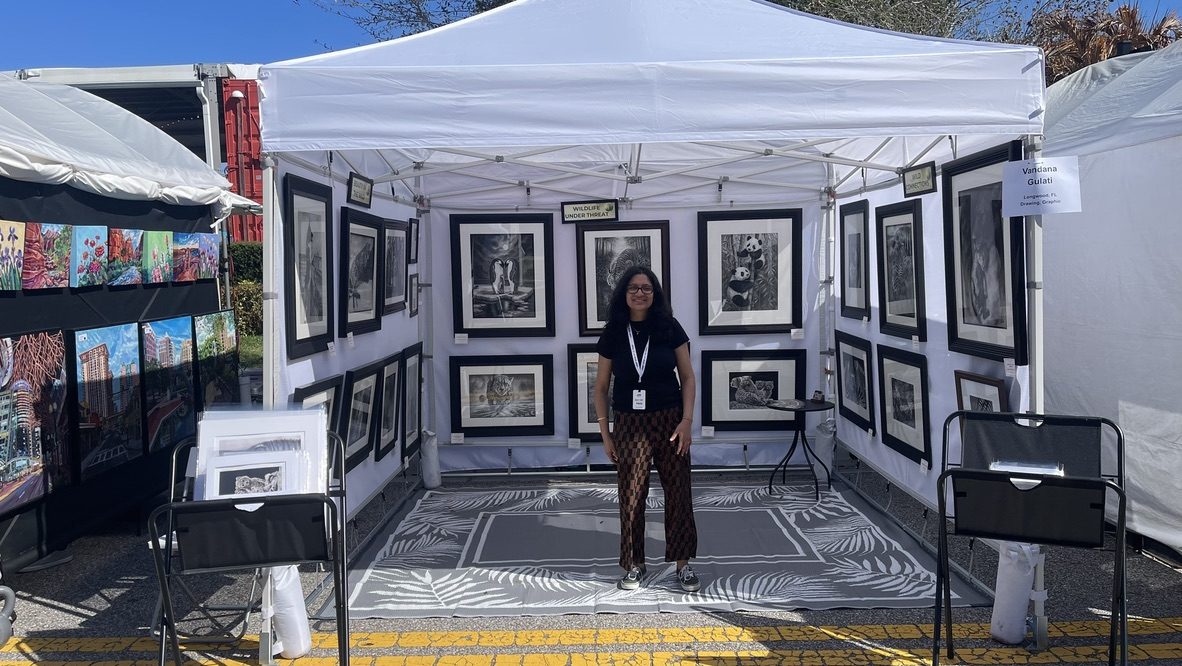 The artist standing proudly in her booth surrounded by framed graphite wildlife drawings