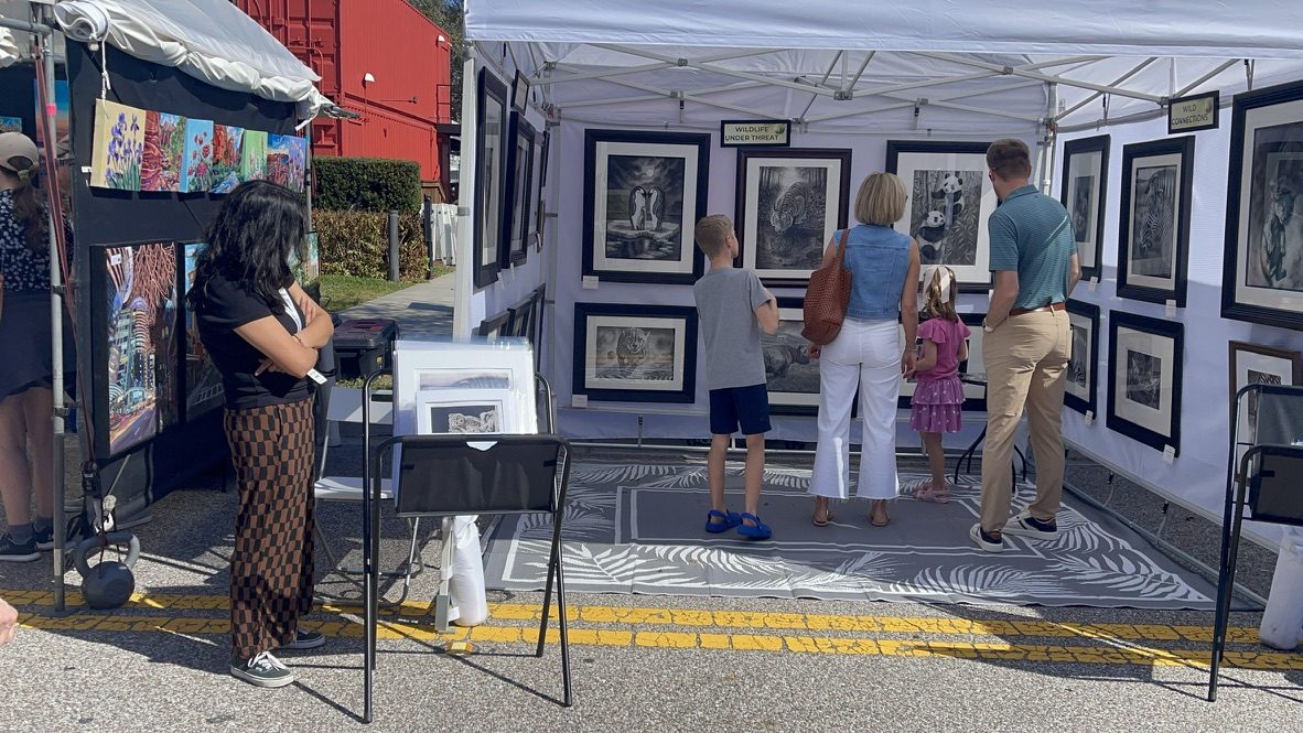 A family stops to view framed wildlife drawings at a festival booth